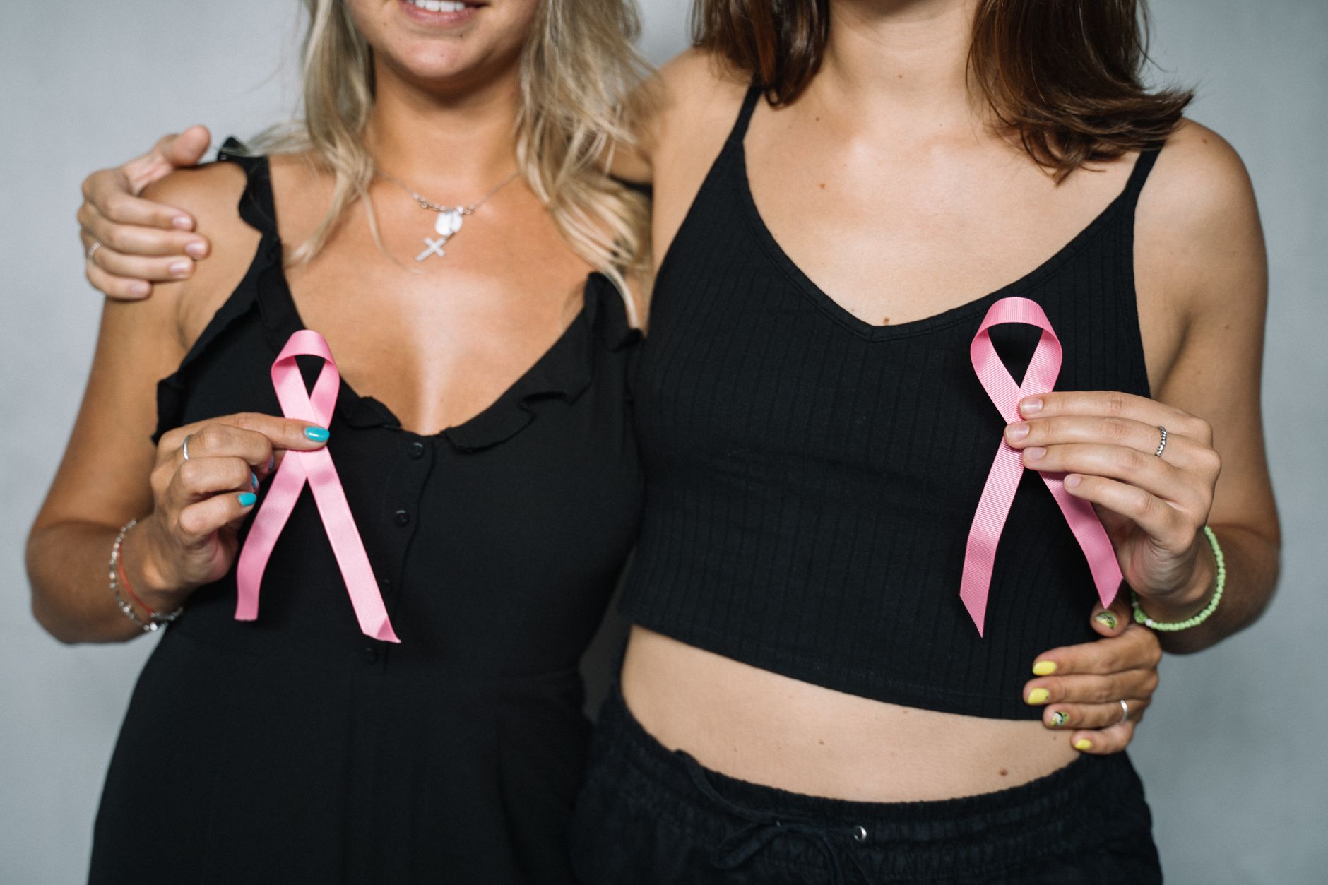 Two women showing support for breast cancer awareness by holding pink ribbons.